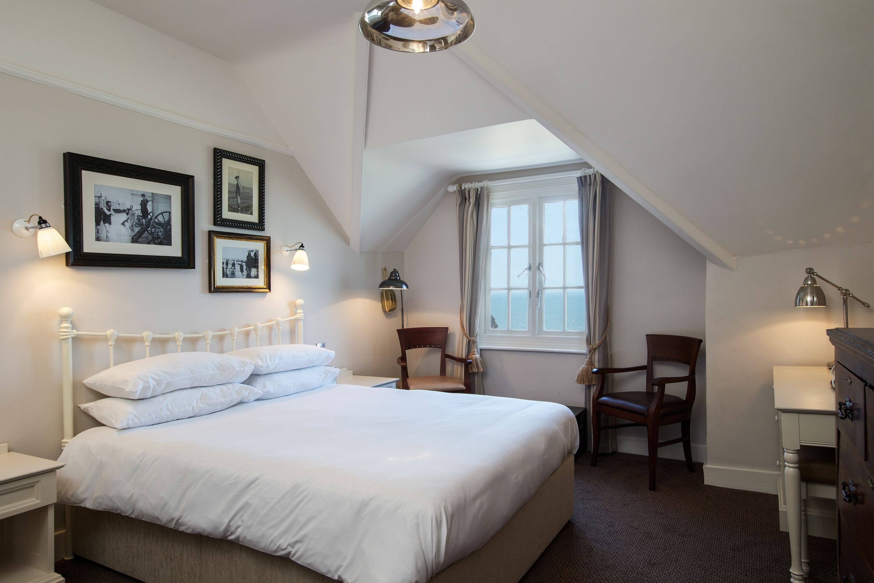 A neatly arranged bedroom with a large bed, two chairs, a desk, and framed pictures on the wall.