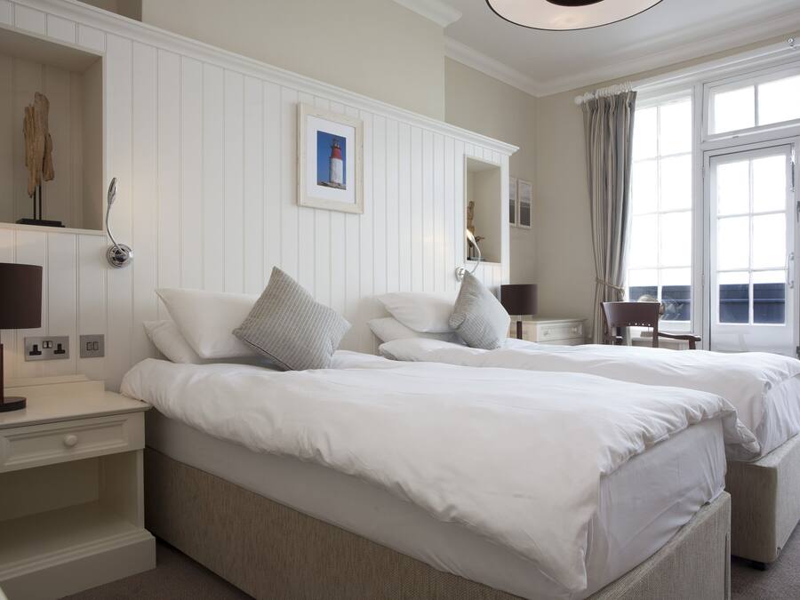 A hotel room with two beds, a nightstand with a lamp, a framed picture on the wall, and a large window with curtains.