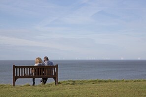 A couple sitting on a bench overlooking a body of water with wind turbines in the distance. - Marine Hotel (Whitstable)