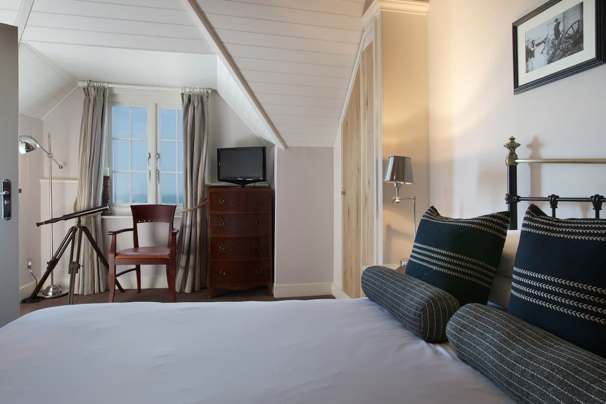 A hotel room with a bed, a chair, a dresser, a television, and a window with curtains.