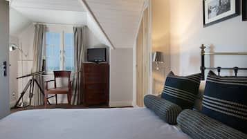 A hotel room with a bed, a chair, a dresser, a television, and a window with curtains.