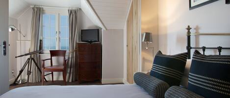 Una habitación de hotel con cama, una silla, cómoda, televisor y ventana con cortinas.