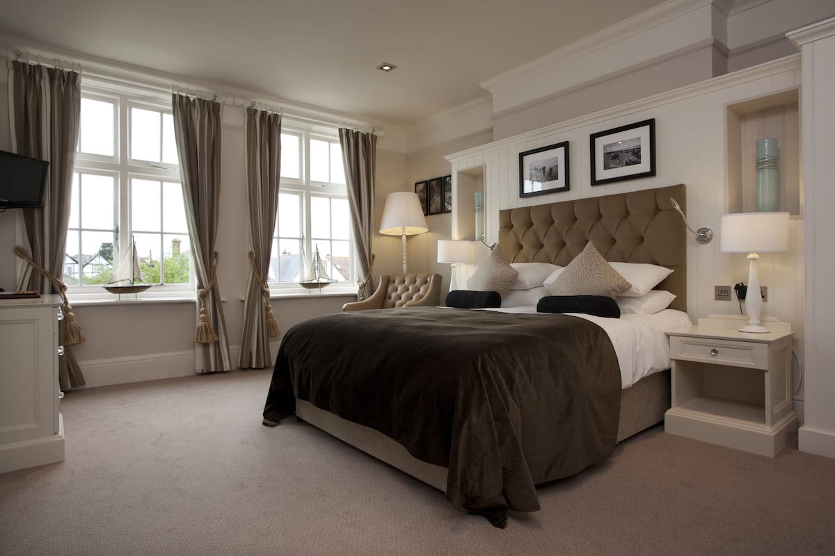 A spacious bedroom with a large bed, two bedside tables with lamps, a TV on the left, and a window with curtains.