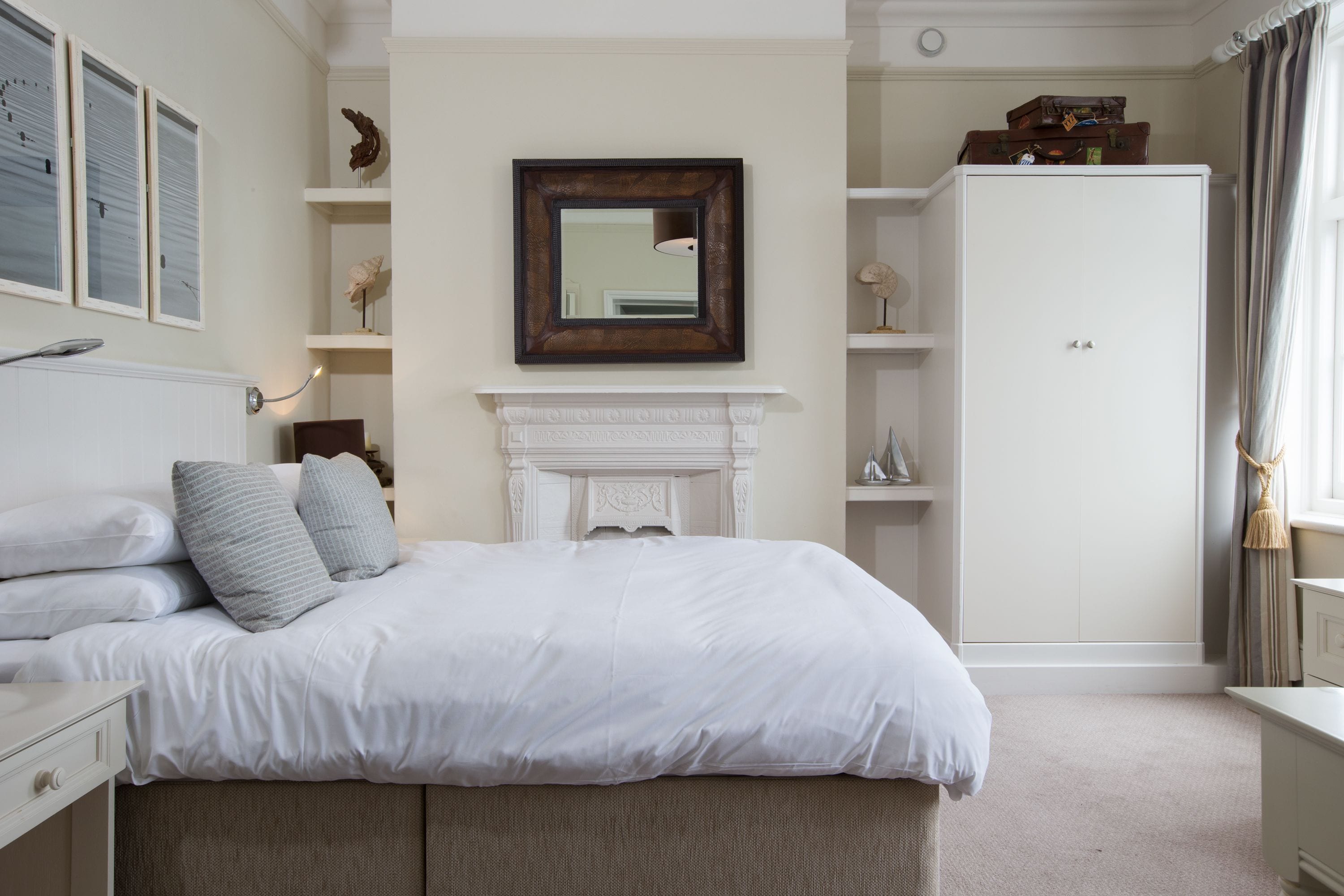A bedroom with a large bed, a white dresser, a wardrobe, a fireplace, and a mirror on the wall.