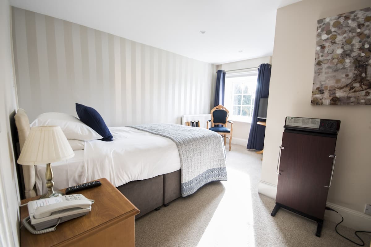 A hotel room with a bed, bedside table with a lamp and phone, a small cabinet, and a window with curtains.