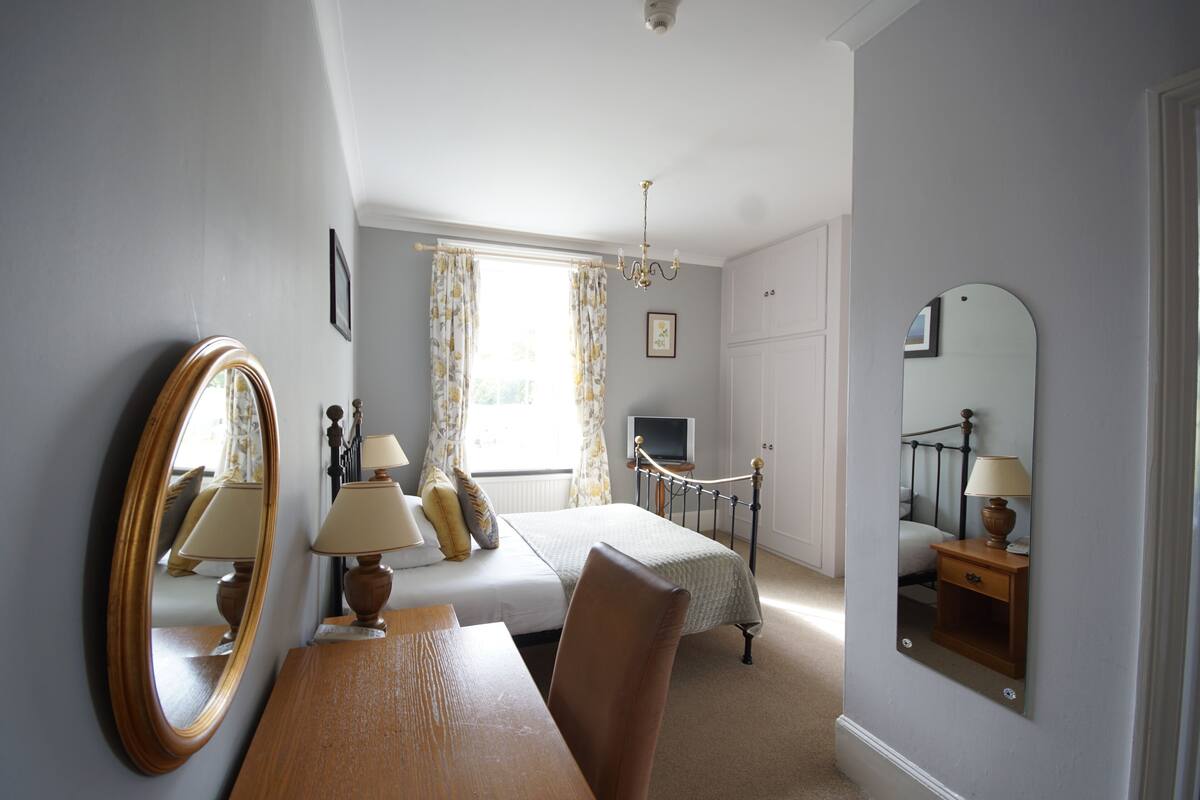 A hotel room with a bed, bedside table, chair, and a large mirror.