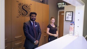 A reception area with a wooden cabinet featuring a decorative letter 'S', a flat-screen TV mounted on the wall, and a counter displaying a London bus tour brochure. - St. George' s Inn Victoria (London)