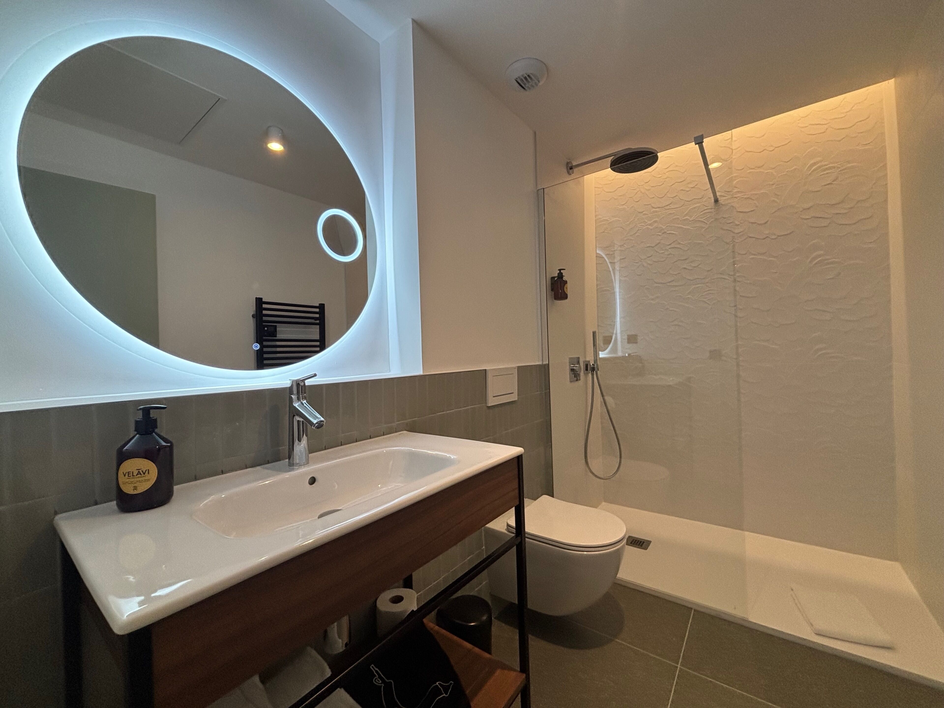 Ein modernes Badezimmer mit rundem Spiegel, Waschbecken, Toilette und Duschkabine.