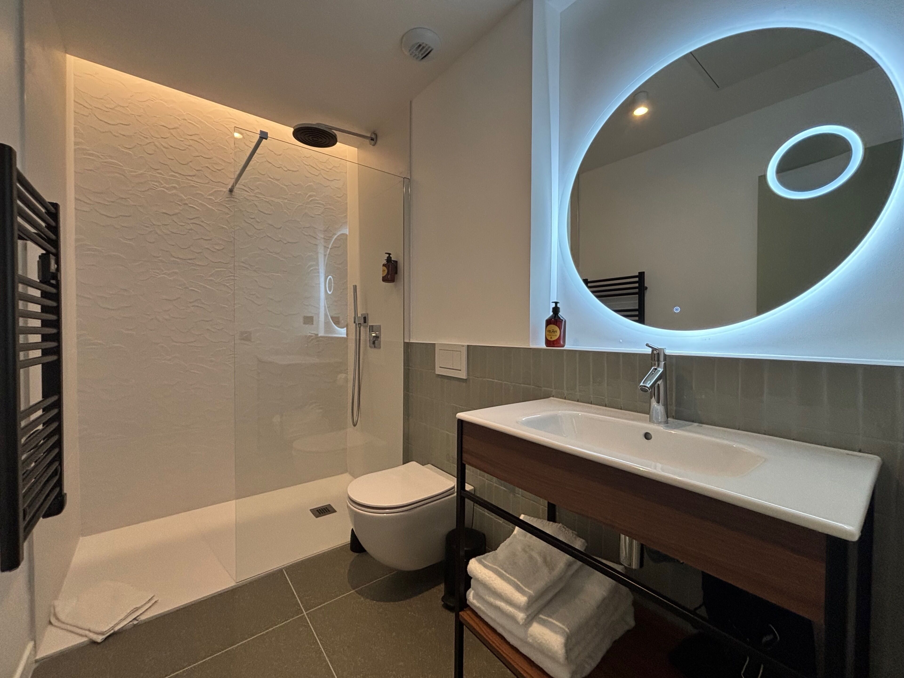 A modern bathroom with a glass-enclosed shower, a white toilet, a sink with a mirror, and a towel rack.