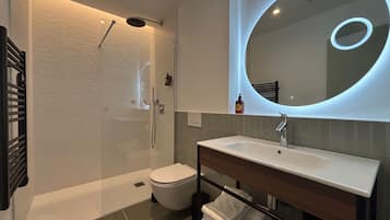 A modern bathroom with a glass-enclosed shower, a white toilet, a sink with a mirror, and a towel rack.
