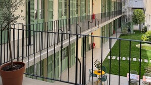 Un edificio de varios pisos con balcones, un patio con mesas y sillas, y una planta en maceta.