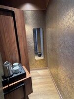 Un baño moderno con tocador de madera, un espejo y una bandeja con hervidor y tazas.