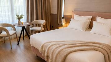 Een hotelkamer met een groot bed, een nachtkastje, een stoel, een kleine tafel met een plant en een spiegel aan de muur.
