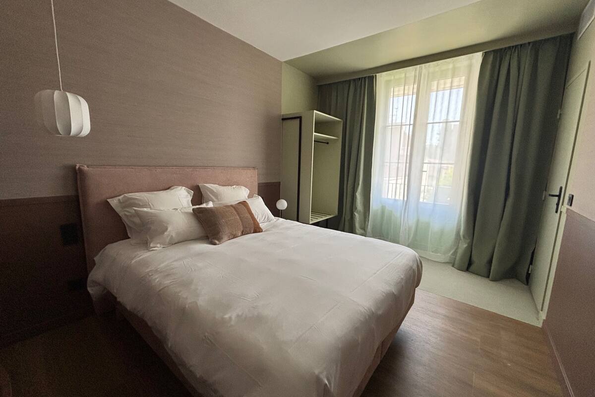 A hotel room with a bed, a bedside table, a mirror, and a window with curtains.
