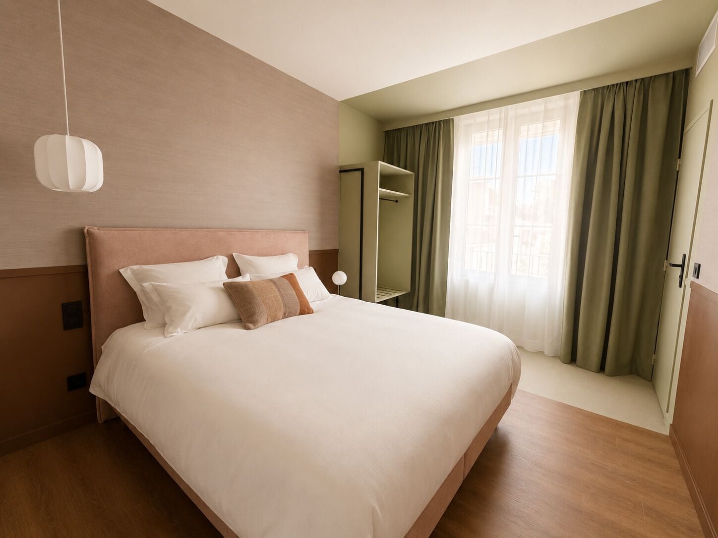 A hotel room with a large bed, a bedside table, a mirror, and a window with curtains.