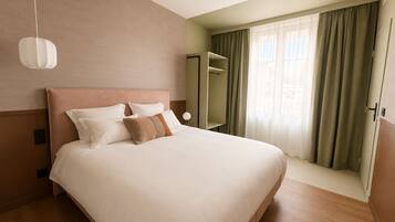 A hotel room with a large bed, a bedside table, a mirror, and a window with curtains.