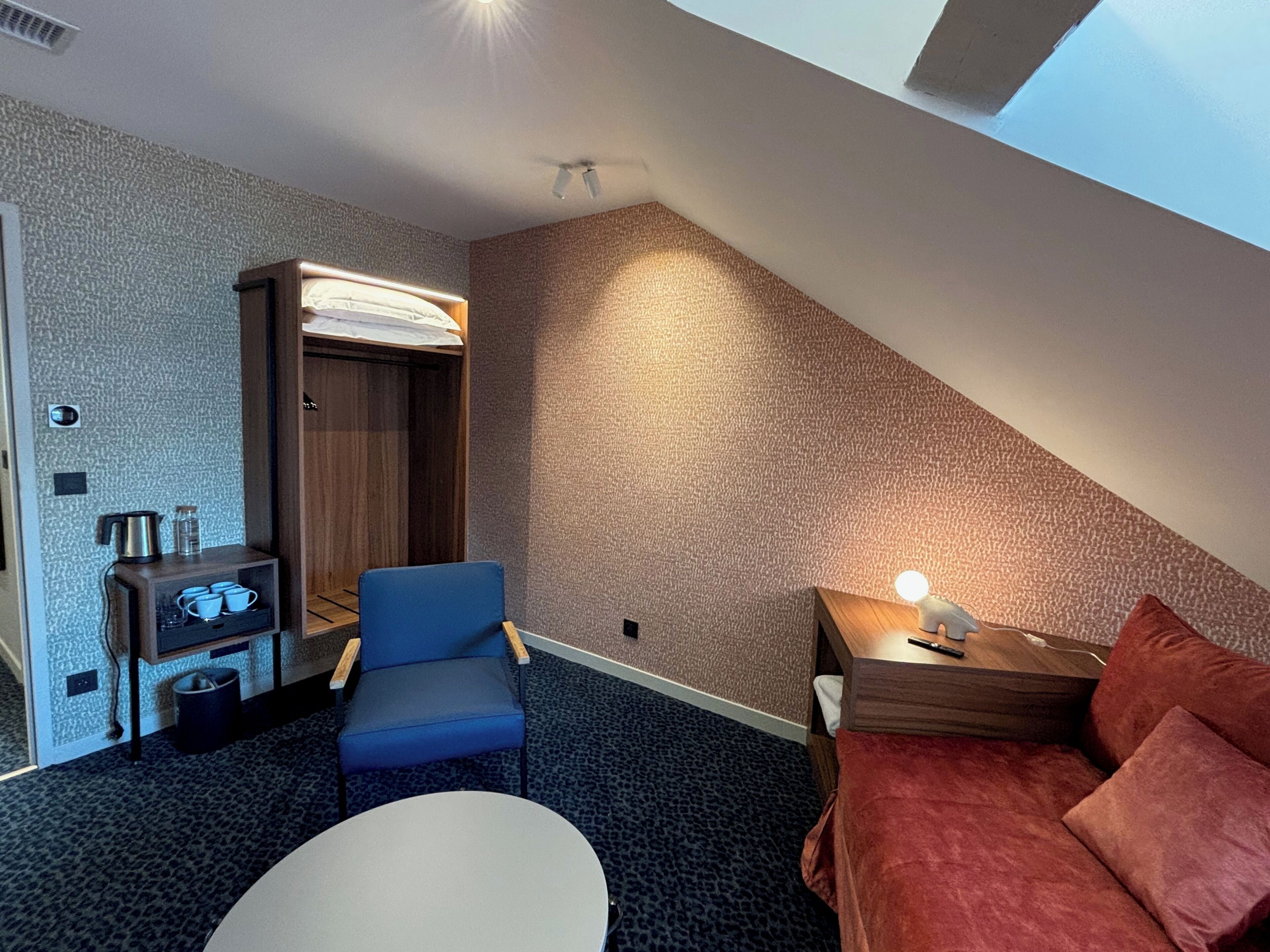 Een hotelkamer met een bed, bureau, stoel, klein tafeltje, kast en lamp.