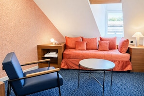 A cozy room with a sofa, a chair, a small table, and a nightstand with a lamp.