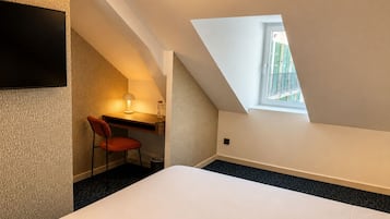 Une chambre à coucher avec un lit, un bureau, une chaise, une lampe et une fenêtre.