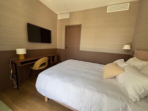 Una habitación de hotel con cama, escritorio, silla, televisión y puerta.