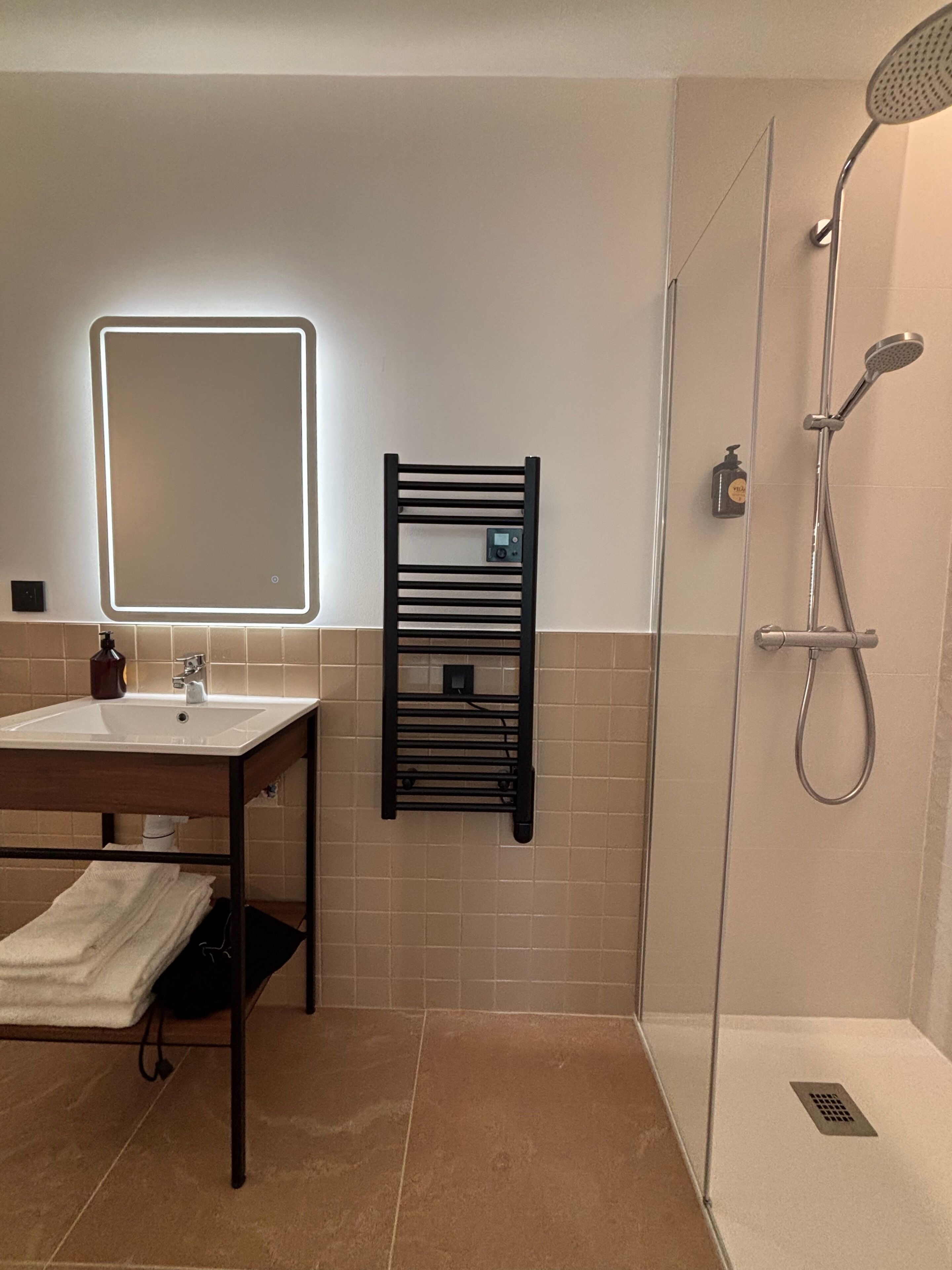 Un baño moderno con lavamanos, espejo, toallero y ducha.