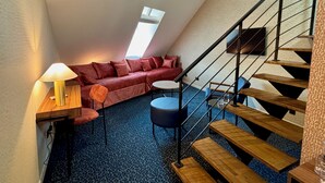 Et loftstudie med en rød sofa, et lille rundt bord, en lampe og en trappe.
