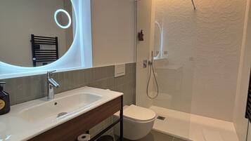 A modern bathroom with a large mirror, a sink, a toilet, and a shower.