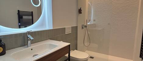 A modern bathroom with a large mirror, a sink, a toilet, and a shower.