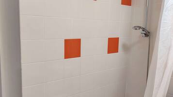 Un baño con azulejos blancos y detalles en naranja, una ducha y un tocador de madera.