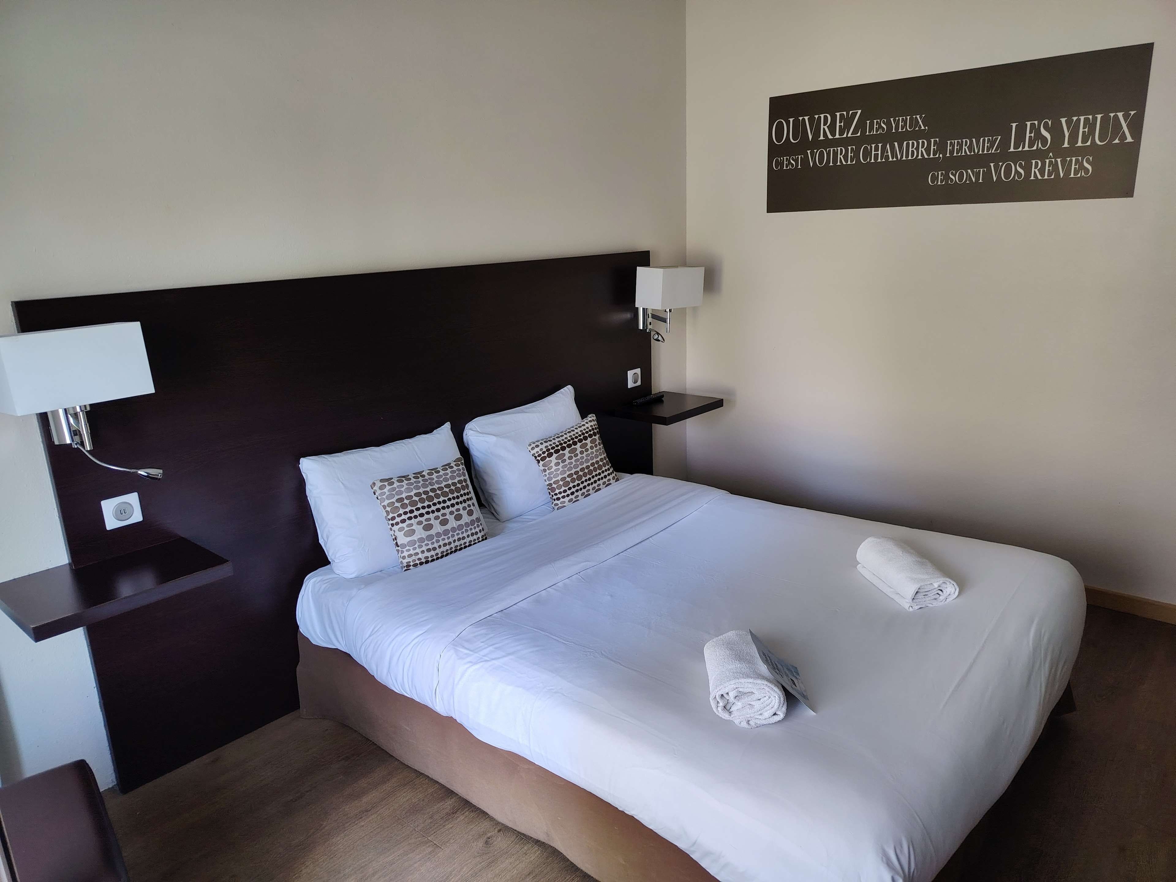 Una habitación de hotel con una cama grande, dos mesitas de noche con lámparas y un cartel en la pared.