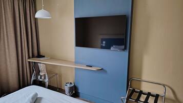 Habitación de hotel con cama, escritorio, silla, televisor y lámpara colgante.