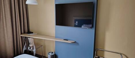 Une chambre d’hôtel comprenant un lit, un bureau avec une chaise, une télévision et un luminaire suspendu.
