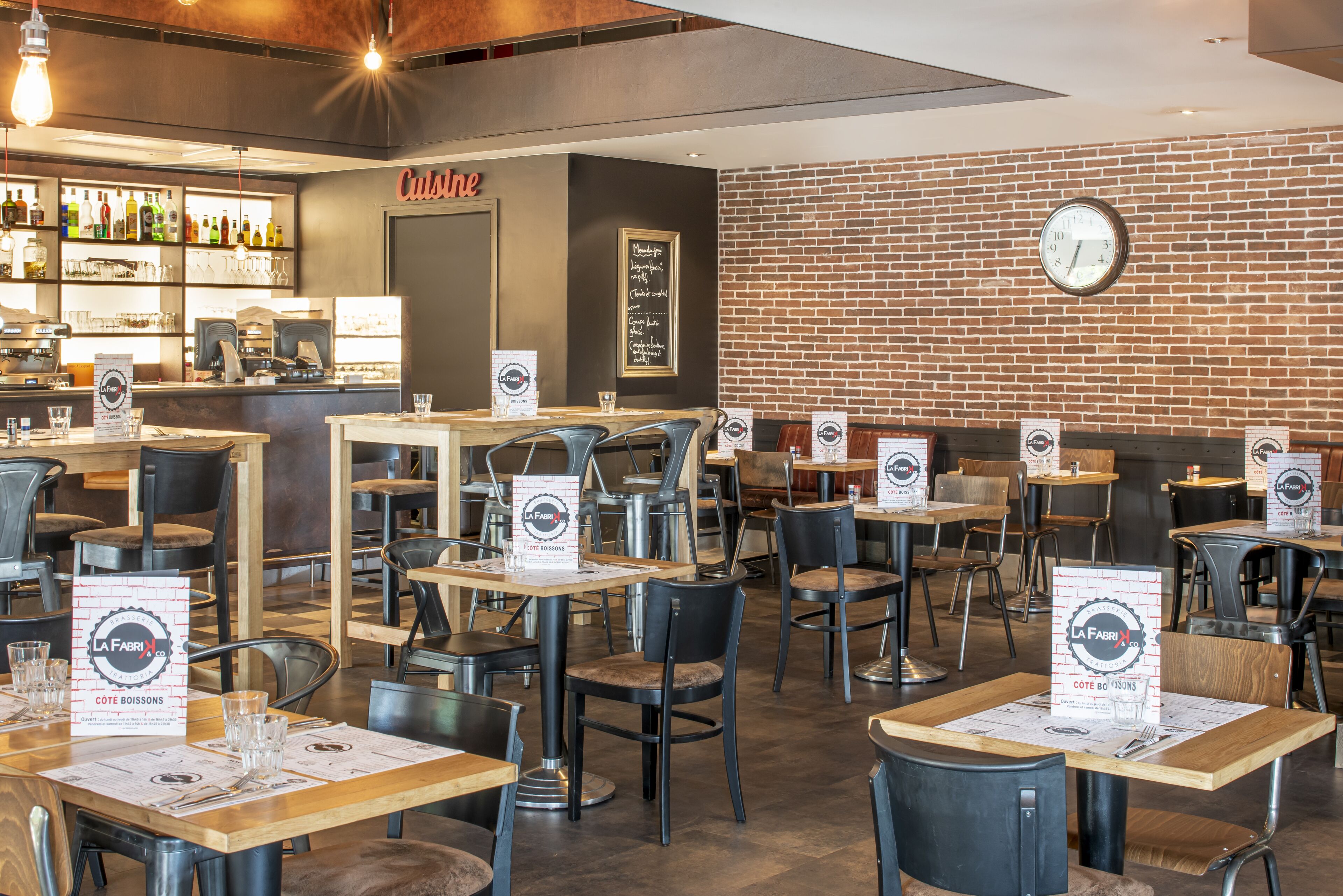 A restaurant interior with tables, chairs, a bar area, and a brick wall.
