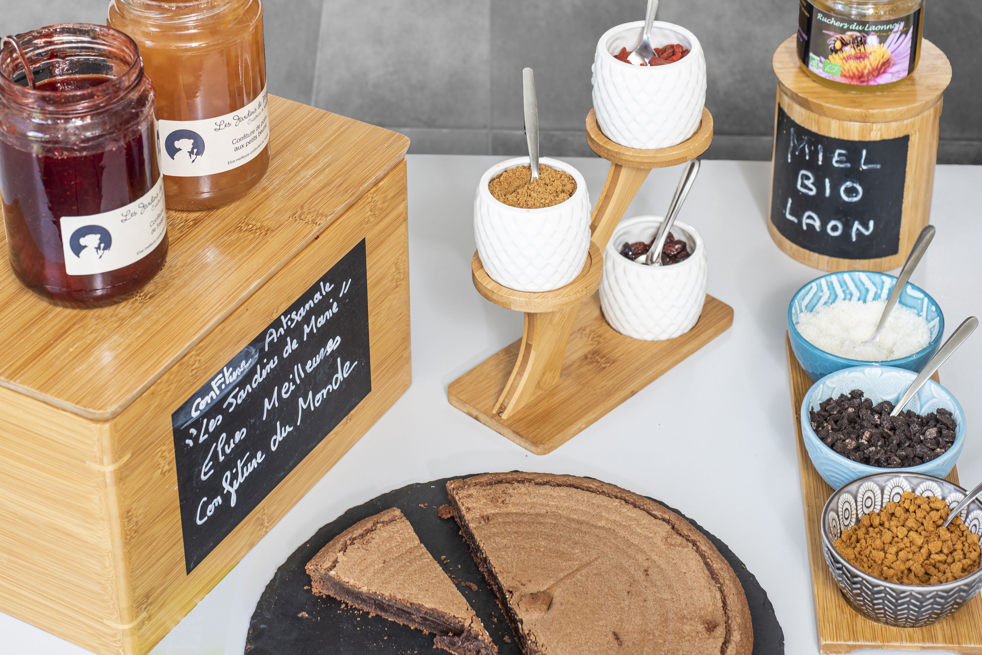 A variety of food items including jars of jam, bowls of chocolate, and a cake on a wooden board.