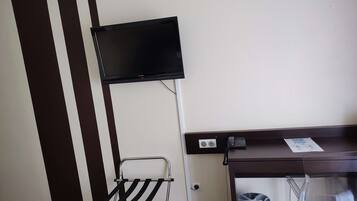 A hotel room with a flat-screen TV mounted on the wall, a desk with a telephone and a paper, and a chair with a black seat.