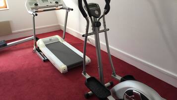Twee stilstaande fitnessapparaten op een rood tapijt in een kamer met witte muren.