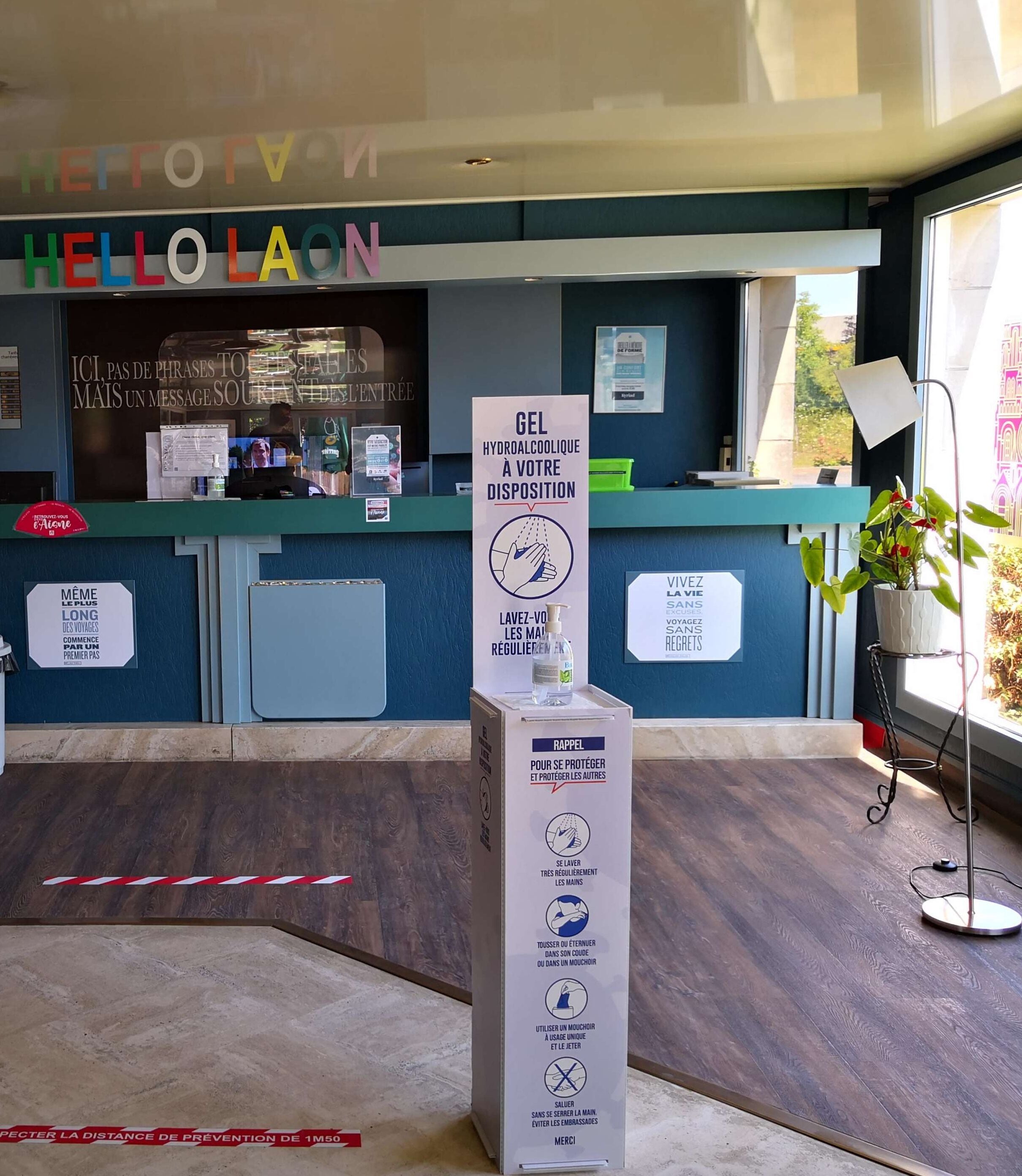 A reception area with a blue counter, a sign offering hand sanitizer, and a sign advising to maintain a 1.5-meter distance.