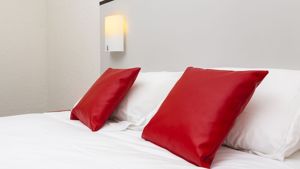 A neatly made bed with white sheets and two red pillows. - Initial by Balladins St Quentin/Gauchy (Gauchy)