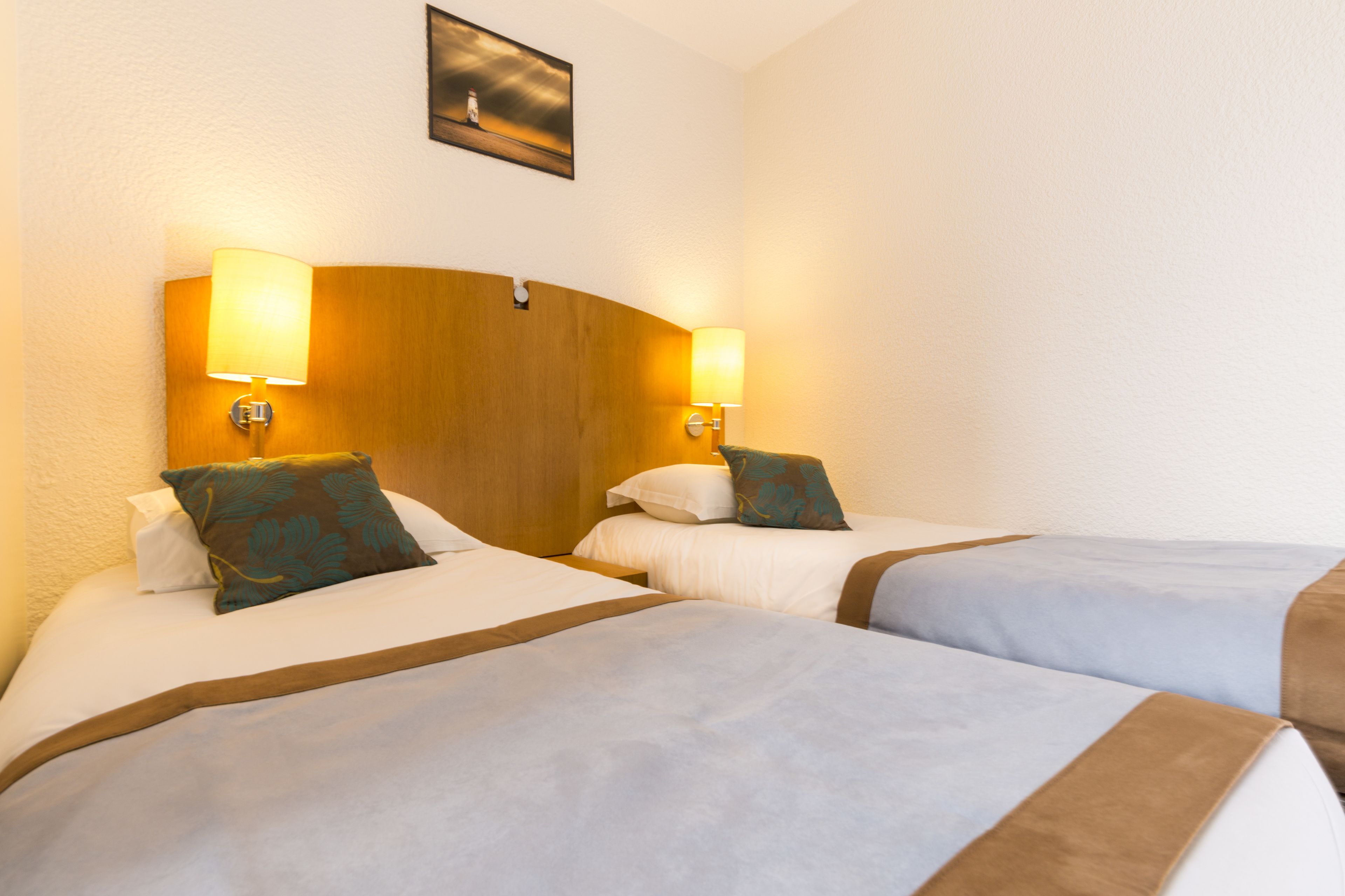 A hotel room with two beds, each with a headboard, bedside lamps, and a painting on the wall.