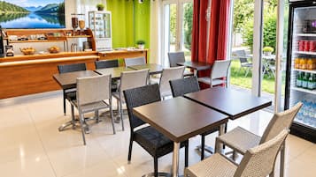 Un restaurante con vistas a un lago, mesas y sillas, una barra con productos alimenticios y un refrigerador con bebidas.