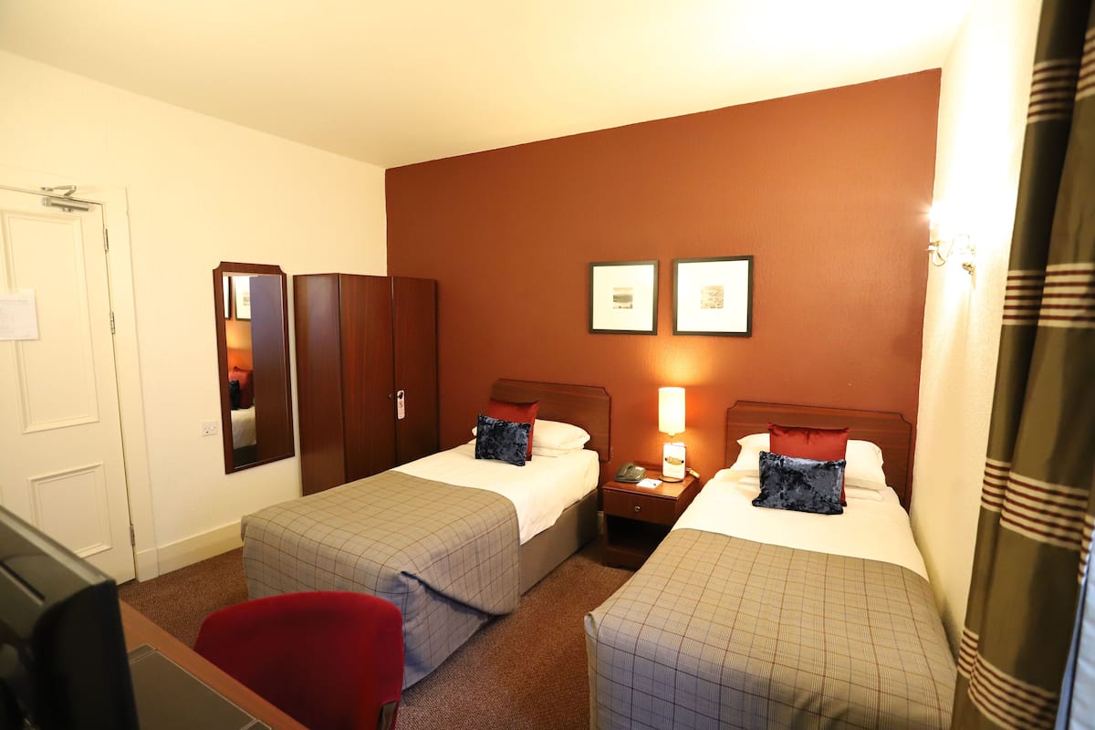 A hotel room with two beds, a desk, a chair, a mirror, and a nightstand.