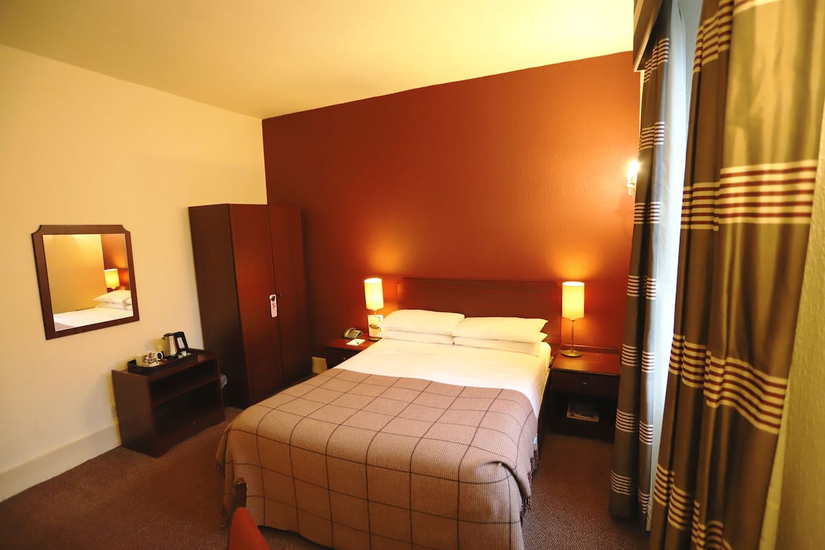 A hotel room with a large bed, two bedside tables with lamps, a wardrobe, a mirror, and a curtain.