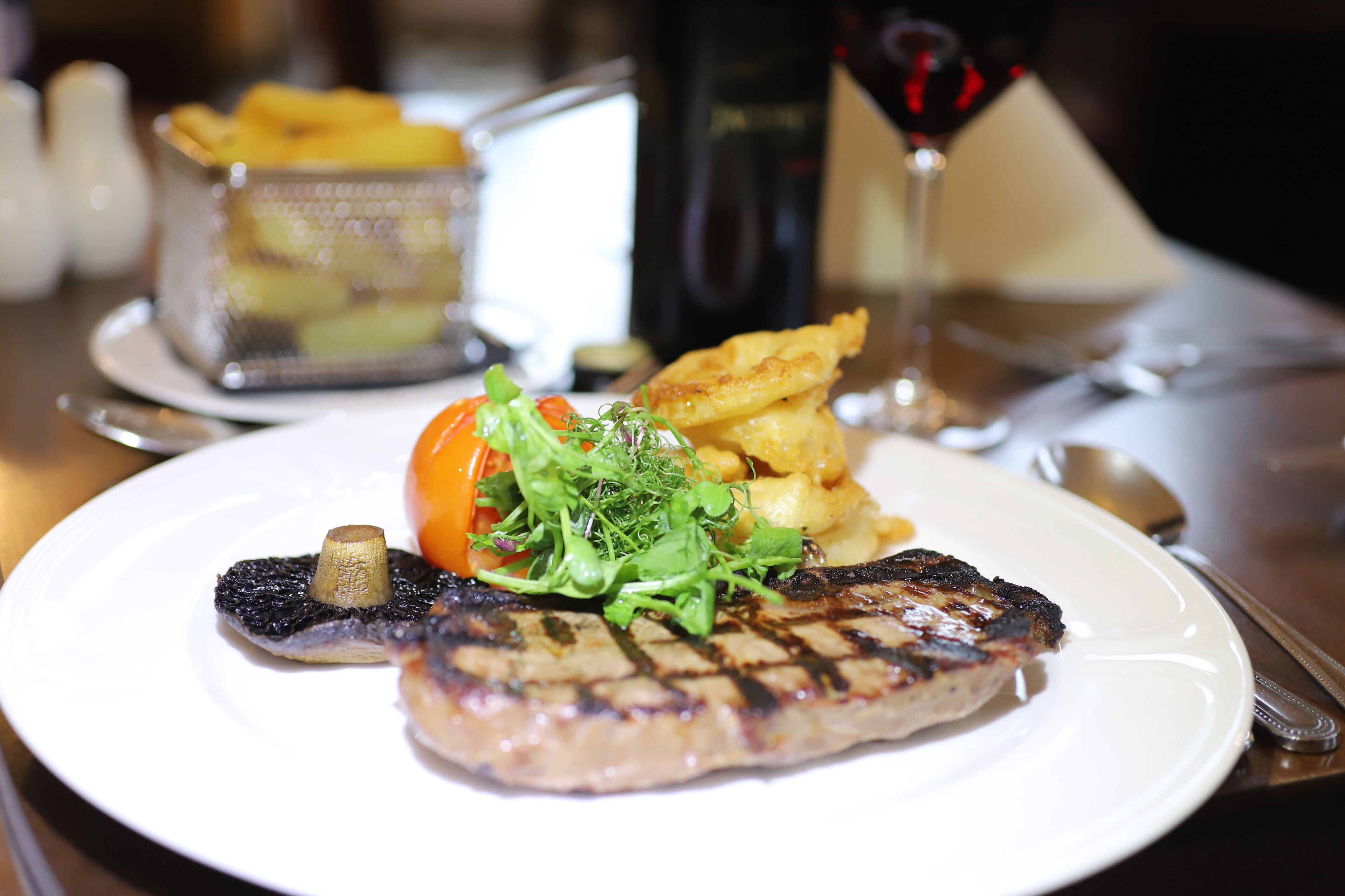 Une assiette contenant de la viande grillée, des frites, une petite salade et un verre de vin rouge, le tout posé sur une table.