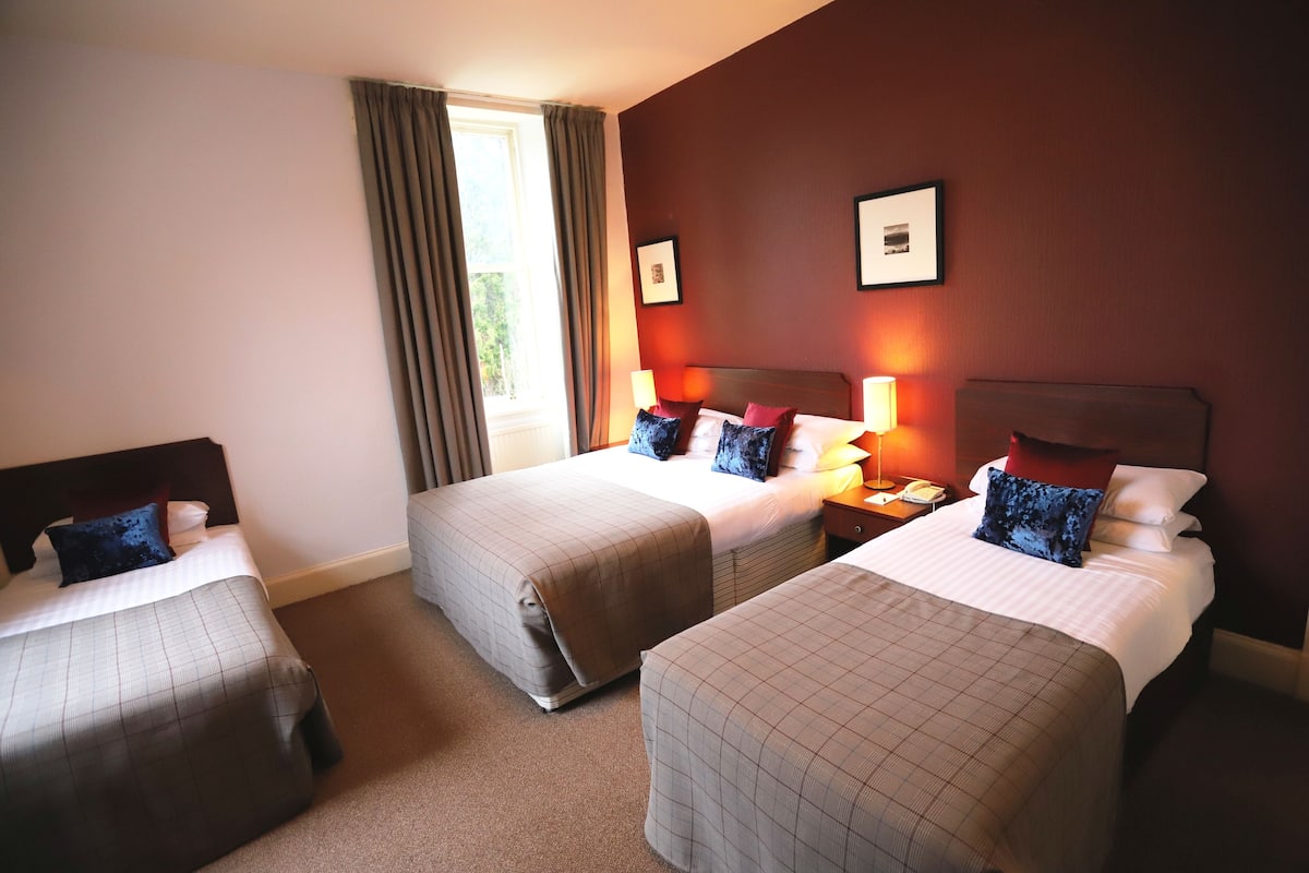 A hotel room with two beds, a window with curtains, and framed pictures on the wall.