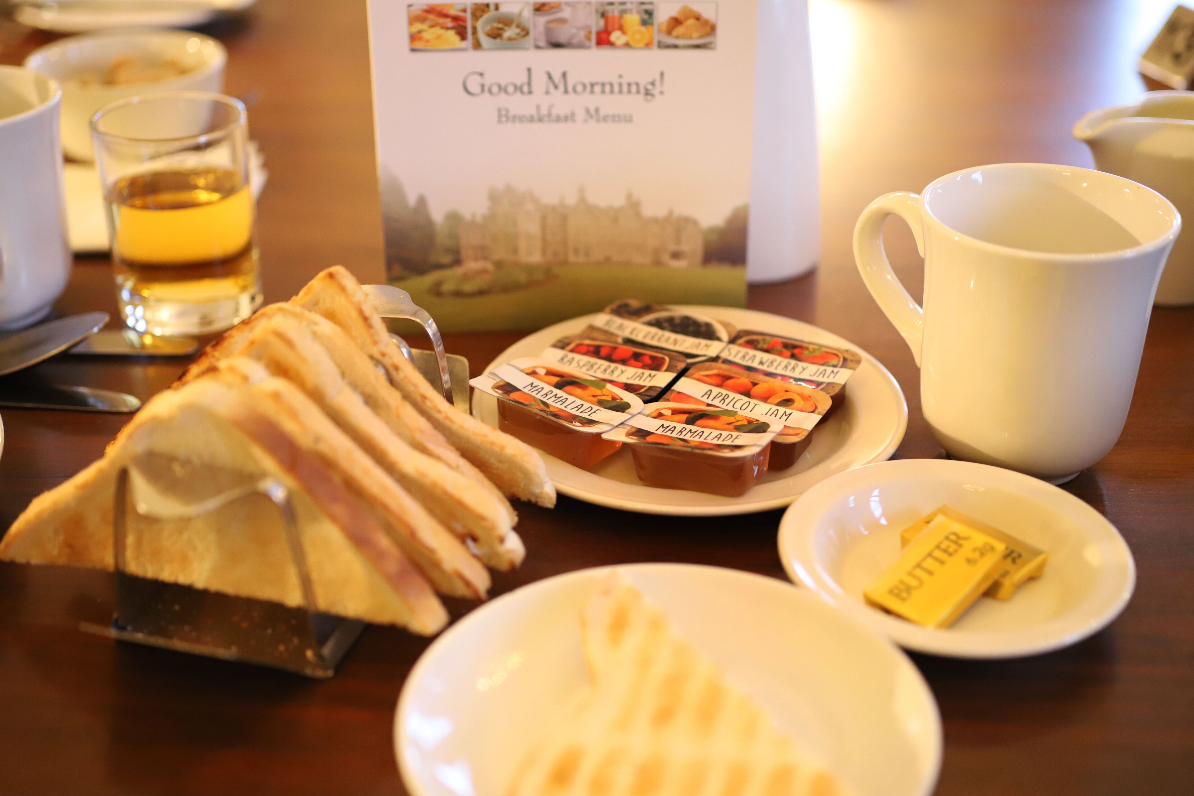 A breakfast setting with a menu, toast, jam, butter, and a mug.