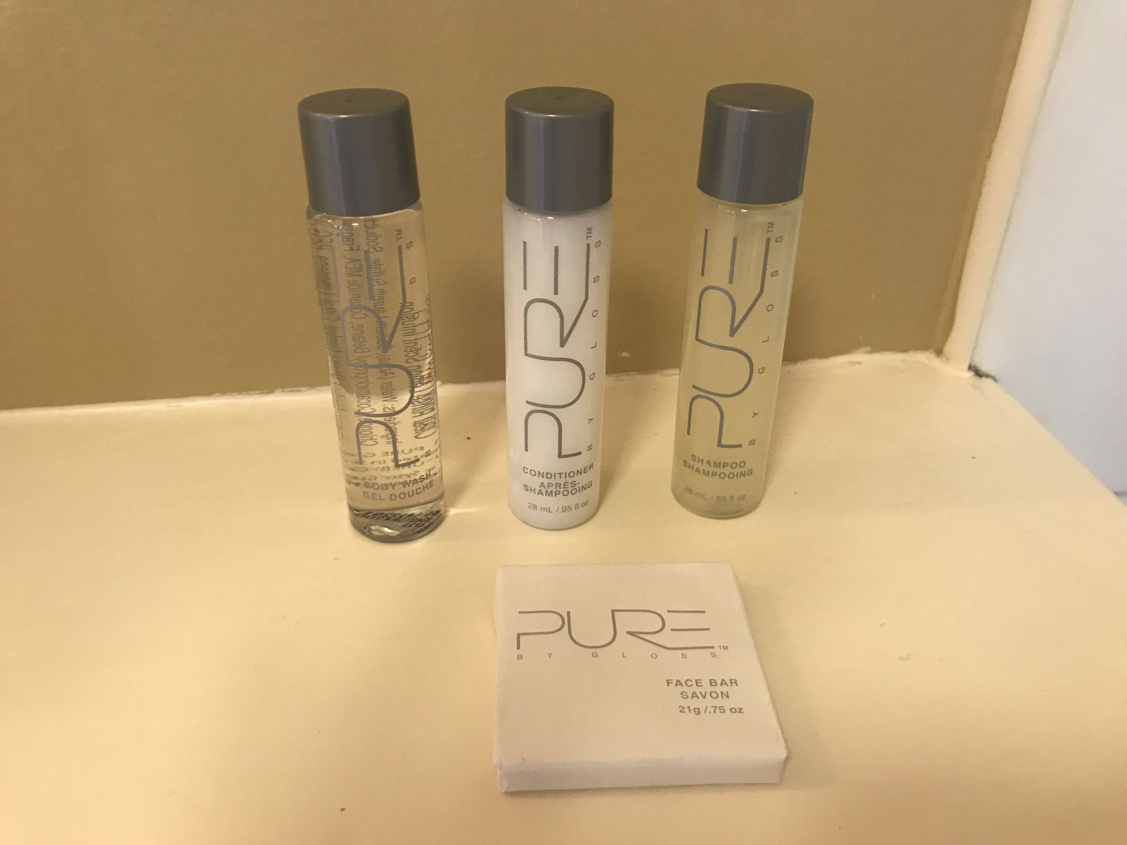 Three bottles of PURE body wash and a face bar on a shelf.