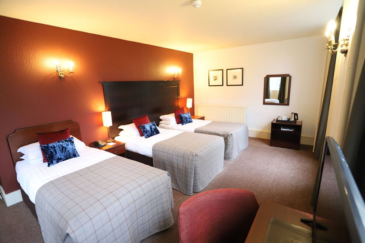 A hotel room with two single beds, a red armchair, a desk with a flat-screen TV, and a mirror on the wall.