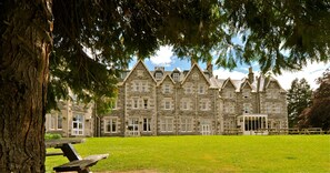 A large stone building with multiple windows and a lawn in front. - Ben Wyvis Hotel (Strathpeffer)