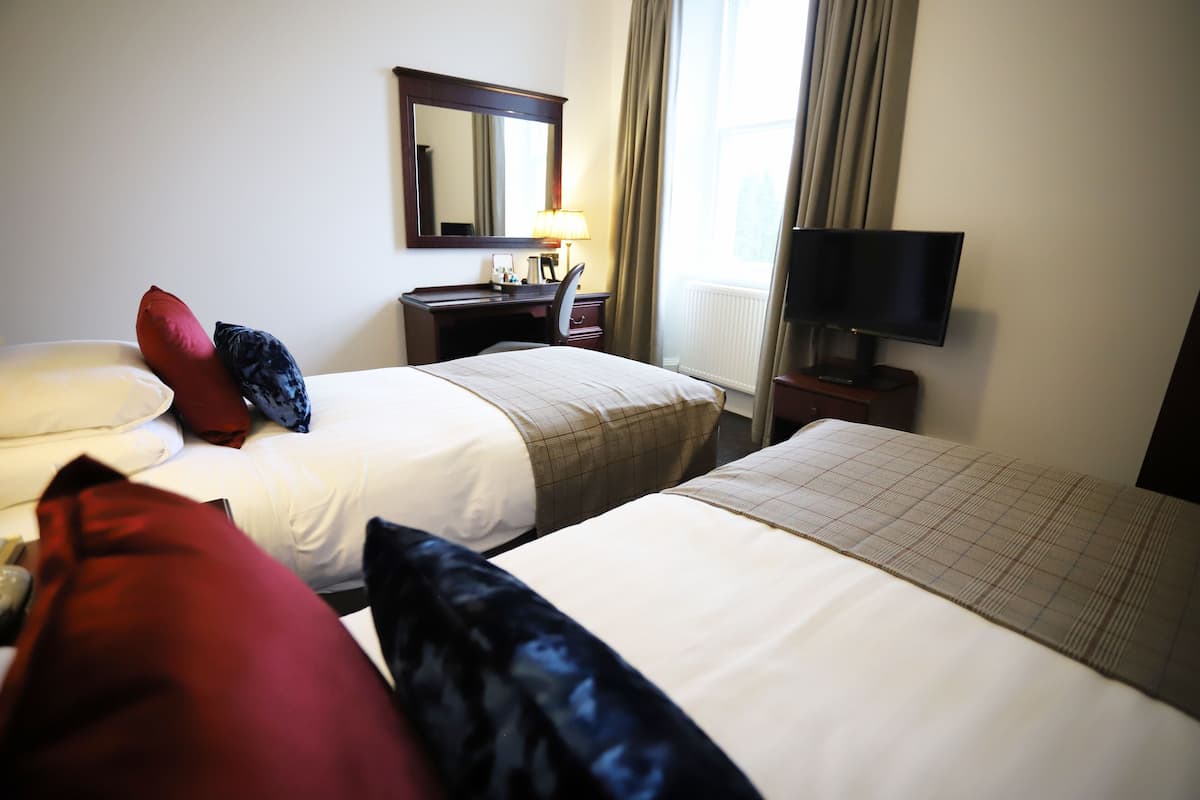 A hotel room with two beds, a desk with a lamp, a TV, and a window with curtains.