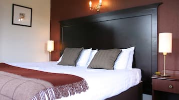 Una cama bien hecha con sábanas blancas y un plaid marrón, un cabecero de madera oscura, dos lámparas de noche y un cuadro en la pared.
